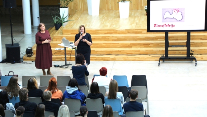 foto ar sievietem kas runā auditorijas priekšā, blakus ekrāns ar uzrakstu ziemeļlatvija