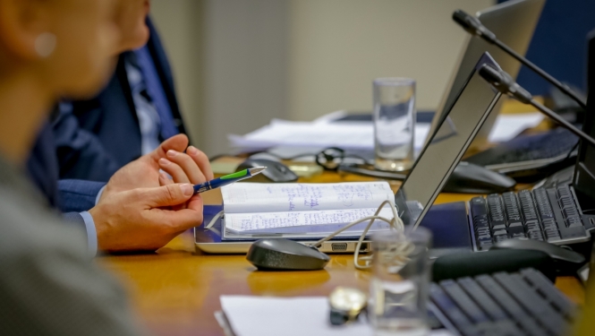 foto ar cilveka rokām, cilveks sež pie galda,rokās pildspalva