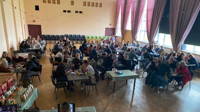 foto cilveki zālē pie galdiņiem 