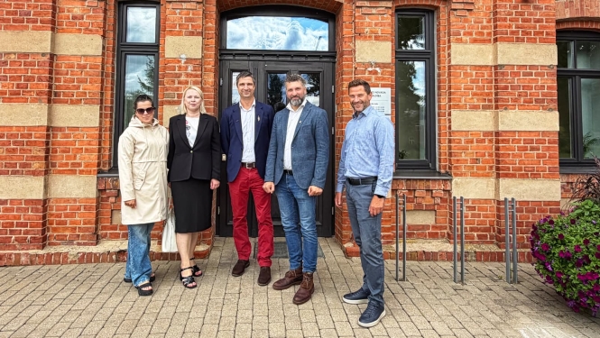 foto ar cilvēkiem kas stāv pie ēkas durvīm