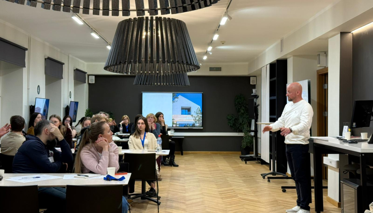 Vīrietis stāv grupas priekšā, pasniedzot informāciju un efektīvi mijiedarbojoties ar auditoriju.