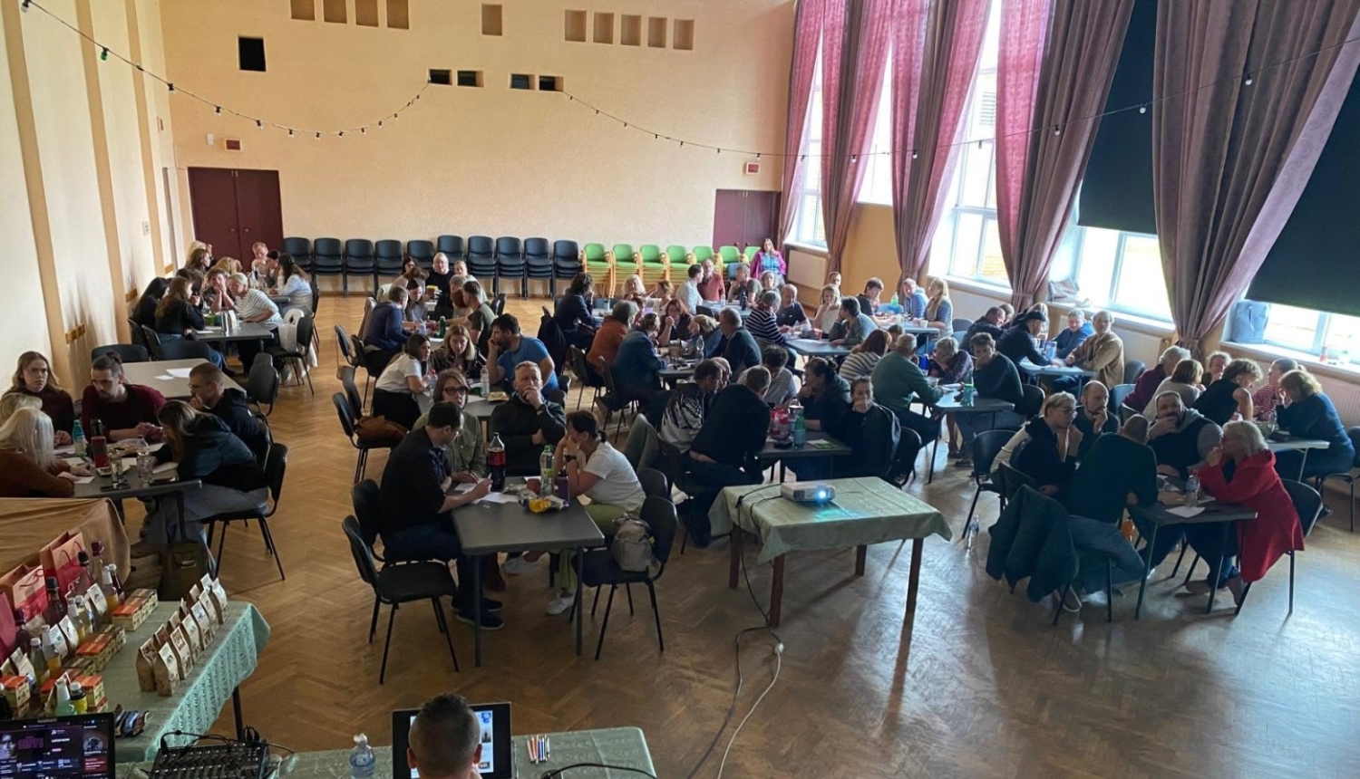 foto cilveki zālē pie galdiņiem 