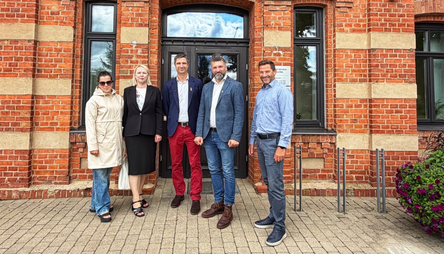 foto ar cilvēkiem kas stāv pie ēkas durvīm