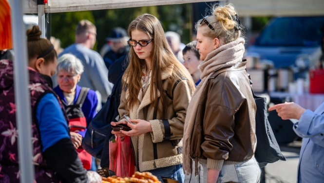 foto ar cilvekiem kas stāv pie tirgotāja gadatirgū