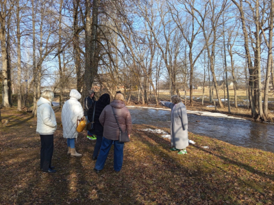 Skolotāji stāv pie upes, vēro dabu 