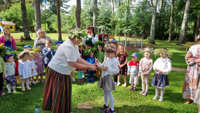 Līgo svētki, audzinātāja tautas tērpā bērnam dod zupiņu ārā