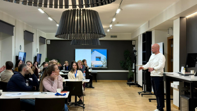 Vīrietis stāv grupas priekšā, pasniedzot informāciju un efektīvi mijiedarbojoties ar auditoriju.