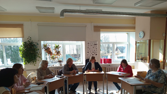 attēlā skolotāji sēž aplī pie galda 