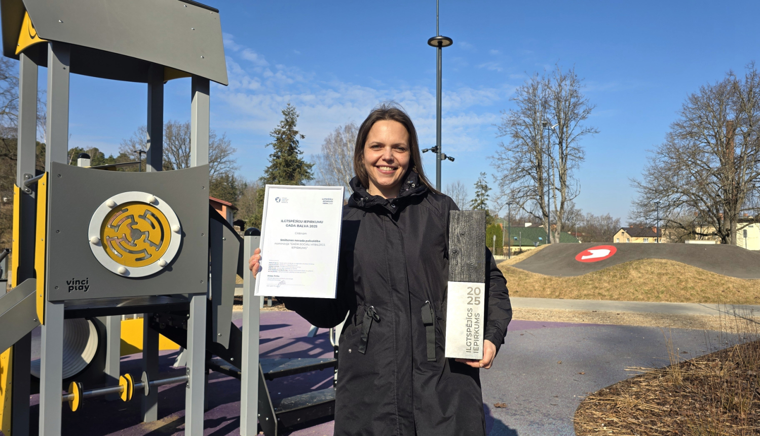 foto ar juridiskās nodaļas pārstāvi aktīvās atpūtas parkā, rokās balva 