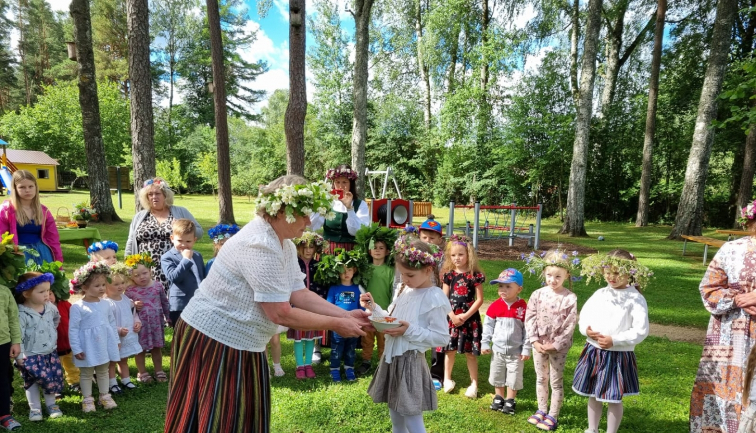 Līgo svētki, audzinātāja tautas tērpā bērnam dod zupiņu ārā