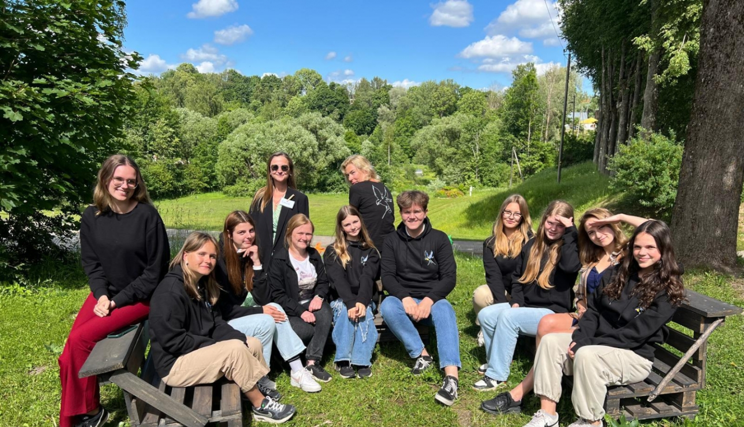 Jaunieši vienā rindā sēž  pie dabas