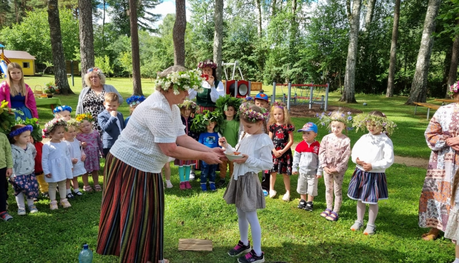Līgo svētki, audzinātāja tautas tērpā bērnam dod zupiņu ārā